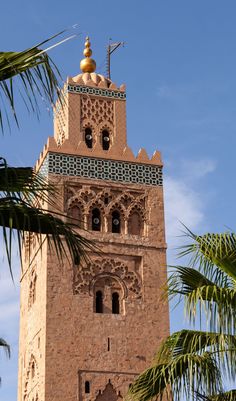 a tall tower with a clock on it's side and palm trees in the foreground