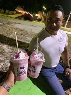 the man is holding two cups with hello kitty ice creams on them and straw sticks sticking out of them