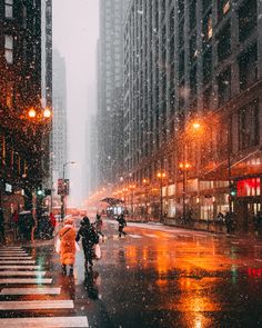 people walking in the rain on a city street at night with umbrellas and buildings