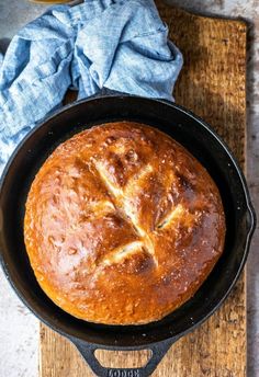 a loaf of bread in a cast iron skillet on a wooden cutting board next to a blue napkin