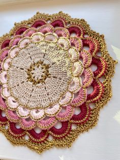 a crocheted doily on a white surface with gold and pink trimmings