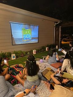 group of people sitting on the grass in front of a screen watching tv at night