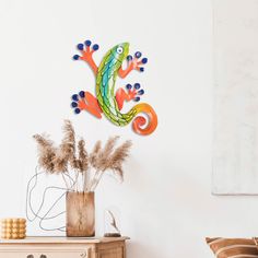 a colorful gecko sitting on top of a wall next to a vase with flowers