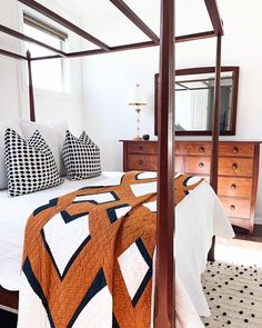 a bed with a quilt on it in a bedroom next to a dresser and mirror