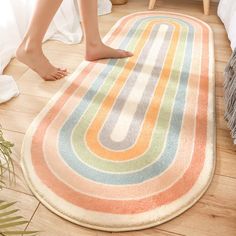 a woman standing on top of a rug next to a white bed and wooden floor