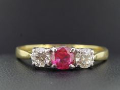 A vibrant Burmese Ruby, Diamond and Gold is a spectacular blend of colours which is graceful with a nod to tradition.  Given as a gift, the Ruby is a symbol of friendship and love. This ring features a 0.57 carat oval cut high quality Burmese Ruby of vibrant mouthwatering hue of cherry red with undertones of candy pinks, this Burmese Ruby really is a true and rare find.   Good cut reflects most of the light that enters it for a quality sparkle. Rubies mined in Burma have long been held as the ab Classic Red Three Stone Diamond Ring, Classic Red Three Stone Rings, Classic Red Three-stone Ring, Heirloom Three Stone Red Rings, Vintage Pink Diamond Ring With Hallmark, Vintage Pink Diamond Ring Hallmarked, Vintage Red Multi-stone Diamond Ring, Vintage Three-stone Ruby Ring Gift, Vintage Three Stone Ruby Ring Gift