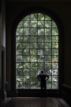 a man standing in front of a large window looking out at the trees behind him