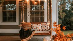 a porch swing with fall leaves on it and lights hanging from the ceiling above it