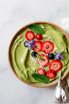 a bowl filled with green smoothie topped with strawberries and blueberries on top