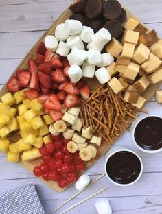 an assortment of fruits and marshmallows on a cutting board with chocolate sauce