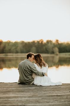 a man and woman sitting on a dock next to the water