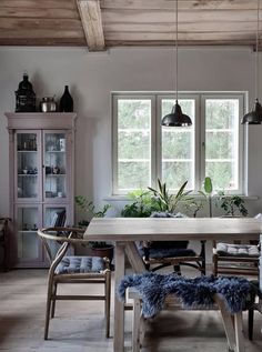 a dining room table and chairs in front of two windows with potted plants on them