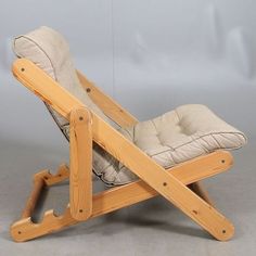 a wooden chair with a cushion on it's back and legs, sitting in front of a gray background