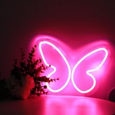 a heart shaped neon sign sitting on top of a table next to a vase with flowers