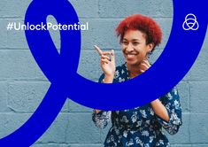 a woman with red hair is smiling and pointing to the side while standing in front of a blue wall