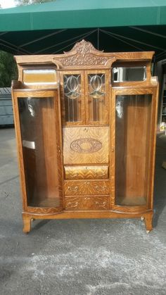 an old wooden cabinet with glass doors on the top and bottom, in front of a green awning