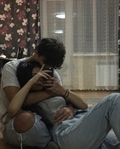 a man and woman sitting on the floor looking at their cell phones