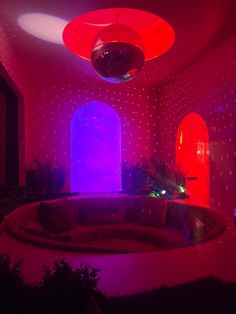 a living room with red and purple lights on the ceiling, round couch in front of an arched window