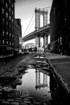 a black and white photo of the manhattan bridge in new york city, with its reflection on the wet pavement