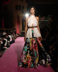 a woman walking down a runway in a white top and multicolored skirt with floral print