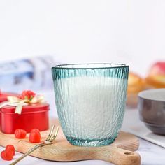 a glass cup sitting on top of a wooden cutting board