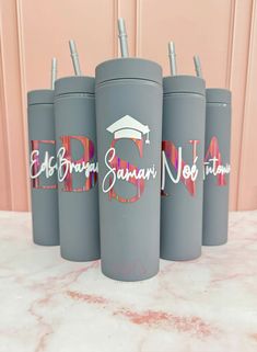 four gray travel mugs with graduation caps and name decals on the side, sitting on a marble countertop