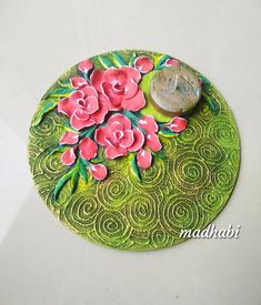 a green plate with pink flowers and a coin on it's side, sitting on a white surface