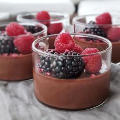 four desserts with raspberries and chocolate pudding in small glass dishes on a table