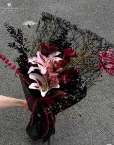 a bouquet of flowers is being held by someone's hand on the street side