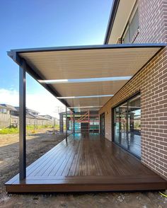 an outdoor covered patio with sliding glass doors and wood flooring on the side of a brick building