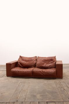 a brown leather couch sitting on top of a wooden floor next to a white wall