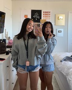 two young women standing next to each other in front of a tv and holding up their cell phones