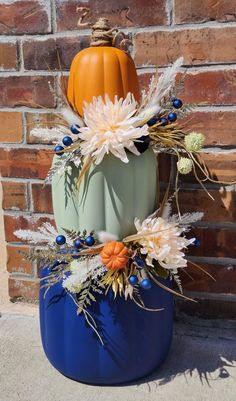 a blue vase with white flowers and orange pumpkins on the top is sitting in front of a brick wall