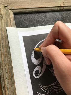 a person holding a pencil in their left hand and drawing on paper with a black marker