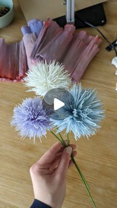 a person is holding some flowers in their hand on a wooden table next to other items