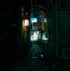 an alley way at night with lights on and signs hanging from the building's sides