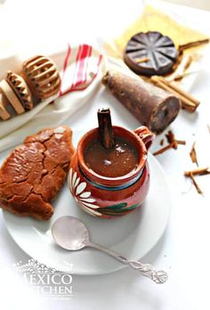 a cup of hot chocolate sits on a plate next to some cinnamon sticks and cookies