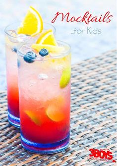 two glasses filled with colorful drinks sitting on top of a woven tablecloth next to each other