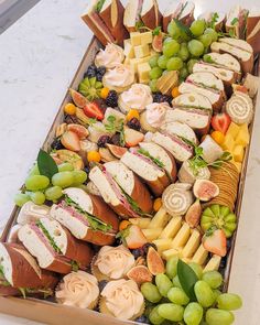 a tray filled with different types of sandwiches and fruit on top of a countertop