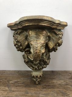 an elephant's head is placed on top of a wooden shelf in front of a white wall