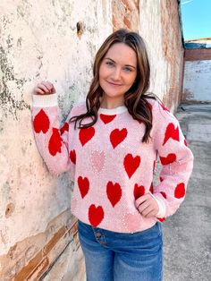 a woman leaning against a wall wearing a sweater with hearts on it