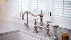 a kitchen sink with two faucets next to a window covered in shutters