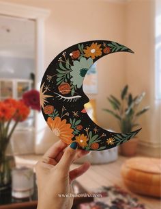 a person holding up a paper cut out of the shape of a crescent with flowers on it