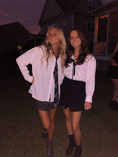 two young women standing next to each other in front of a house at night with their hands on their hips