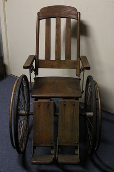 an old fashioned wooden chair with wheels on the floor in front of a white wall