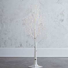 a small white tree with lights on it in front of a wall and concrete floor