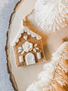 a gingerbread house ornament sitting on top of a piece of wood next to a christmas tree