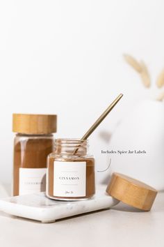 two jars filled with honey sitting on top of a white tray next to a wooden spoon