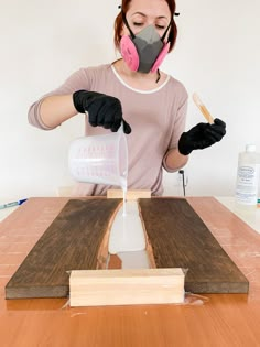 a woman wearing a gas mask and gloves is making a piece of wood with glue