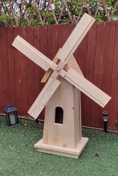 a wooden windmill sitting in the grass next to a fence